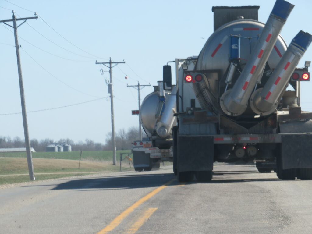 Two waste Hauling Trucks span both lanes of a tired county road
