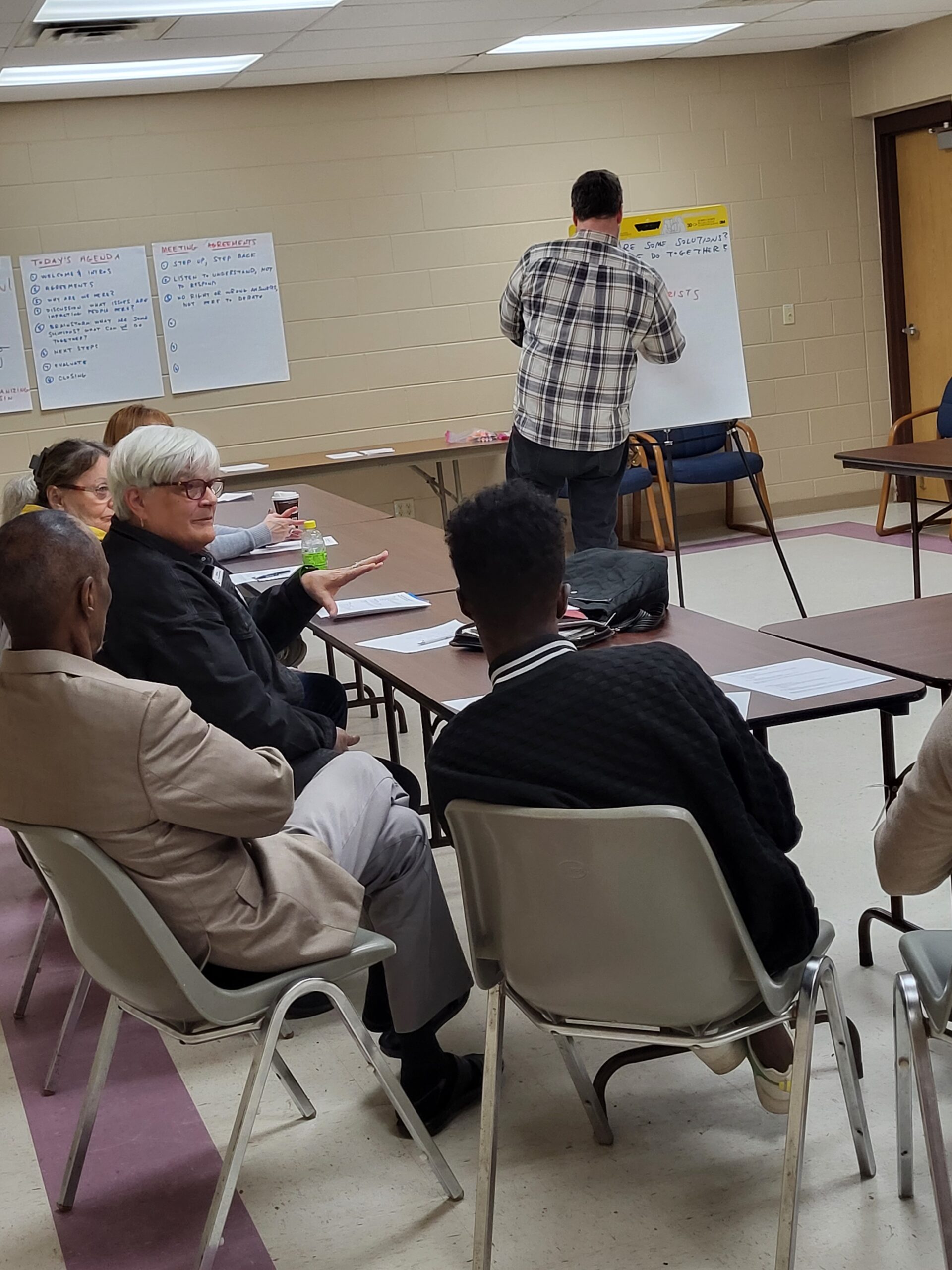 A group sits together at tables in discussion while an organizer takes notes on a large easel pad in a county building in Barron Wisconsin